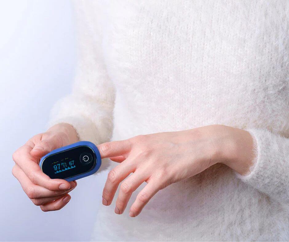 A woman wearing a white sweater places a pulse oximeter on her finger to get a reading.