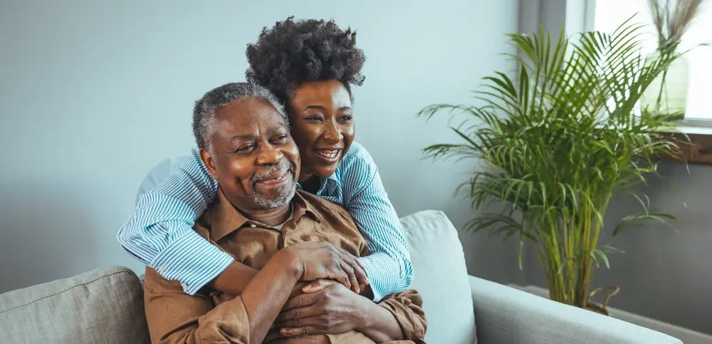 An elderly black couple embrace happily within their home. 